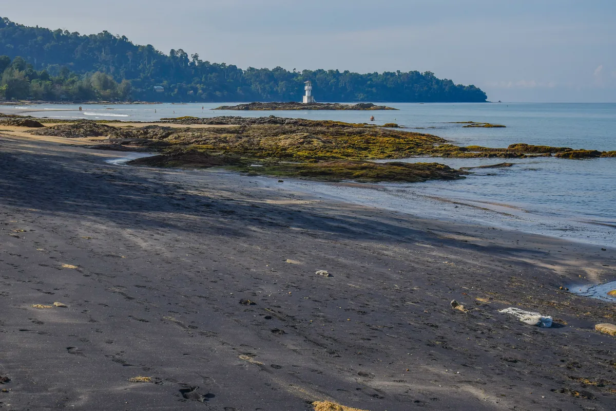 Nang Thong's white light beacon beyond dark rocks and sand