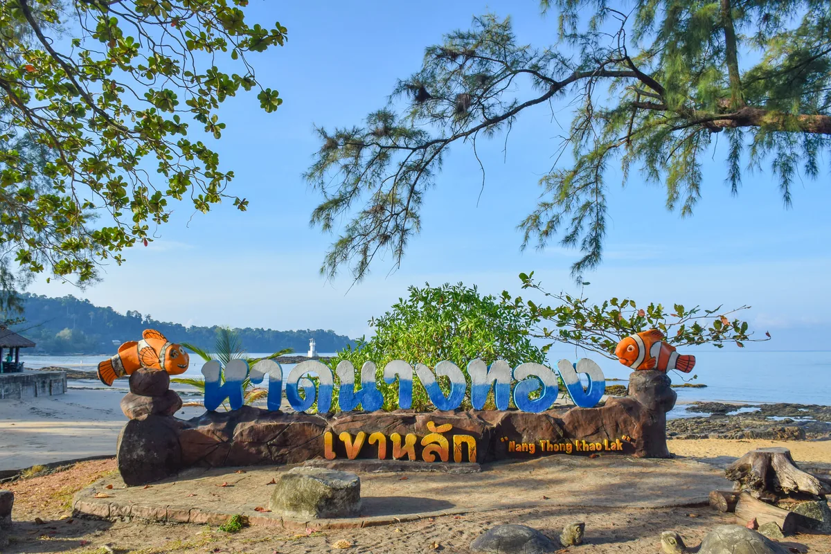 Nang Thong Beach sign beneath trees beside the sea