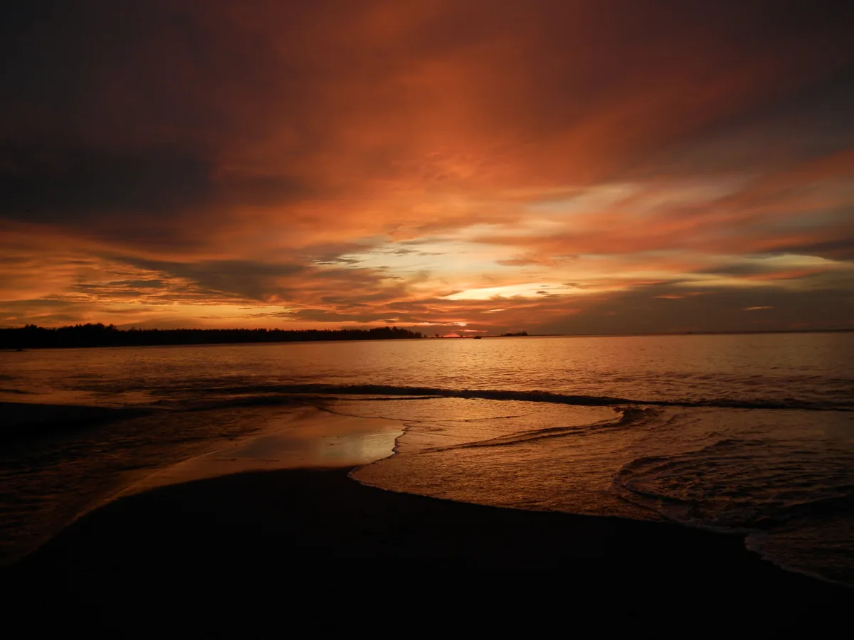 Orange sunset reflected where a coastal stream reaches the sea on Khao Lak's northern shore