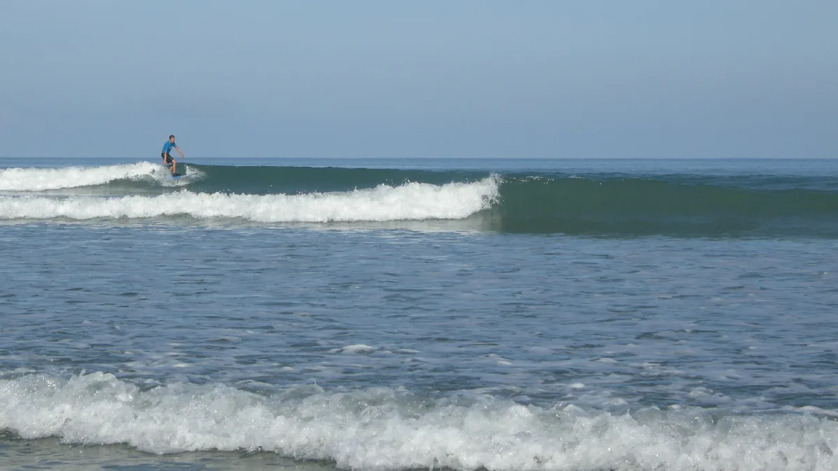 A distant surfer riding a wave offshore at Cape Pakarang