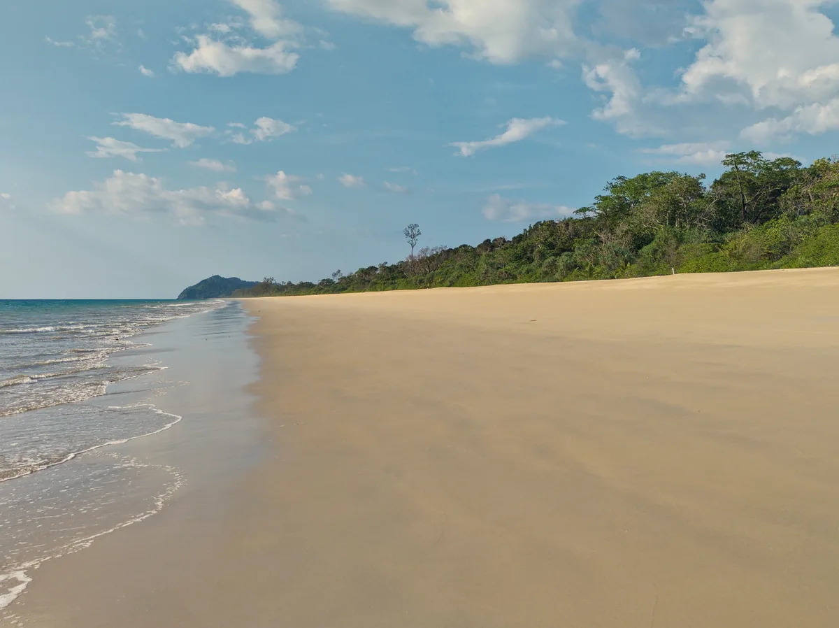 A wide sandy shore and green headland at Thai Mueang Beach