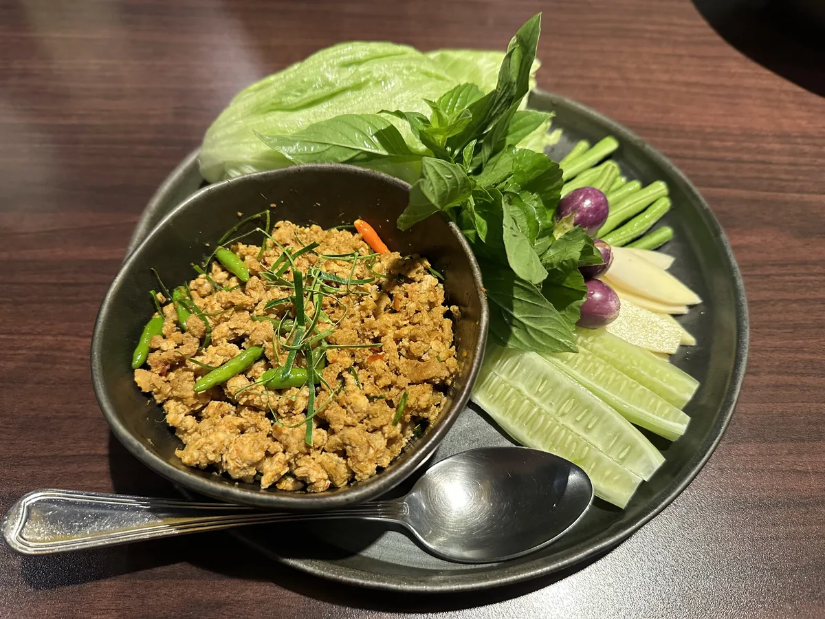 Minced pork khua kling topped with green herbs and chillies beside fresh vegetables