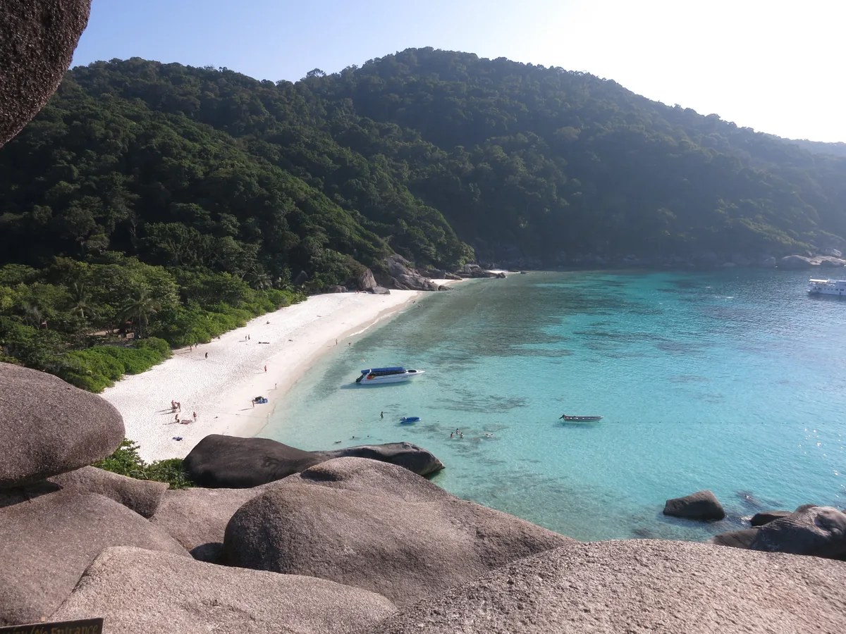 Elevated view of a white beach, forested hill and boats in turquoise water in the Similan Islands