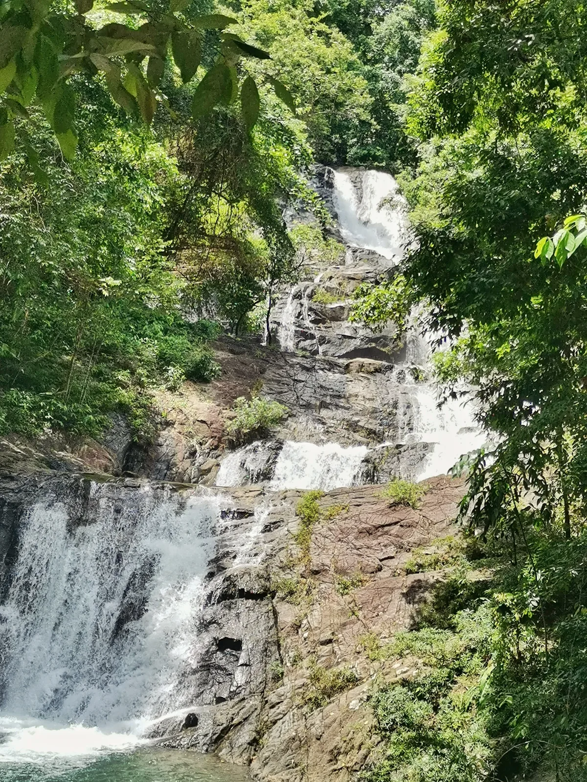 Lampi Waterfall descending over stepped rocks between green forest trees