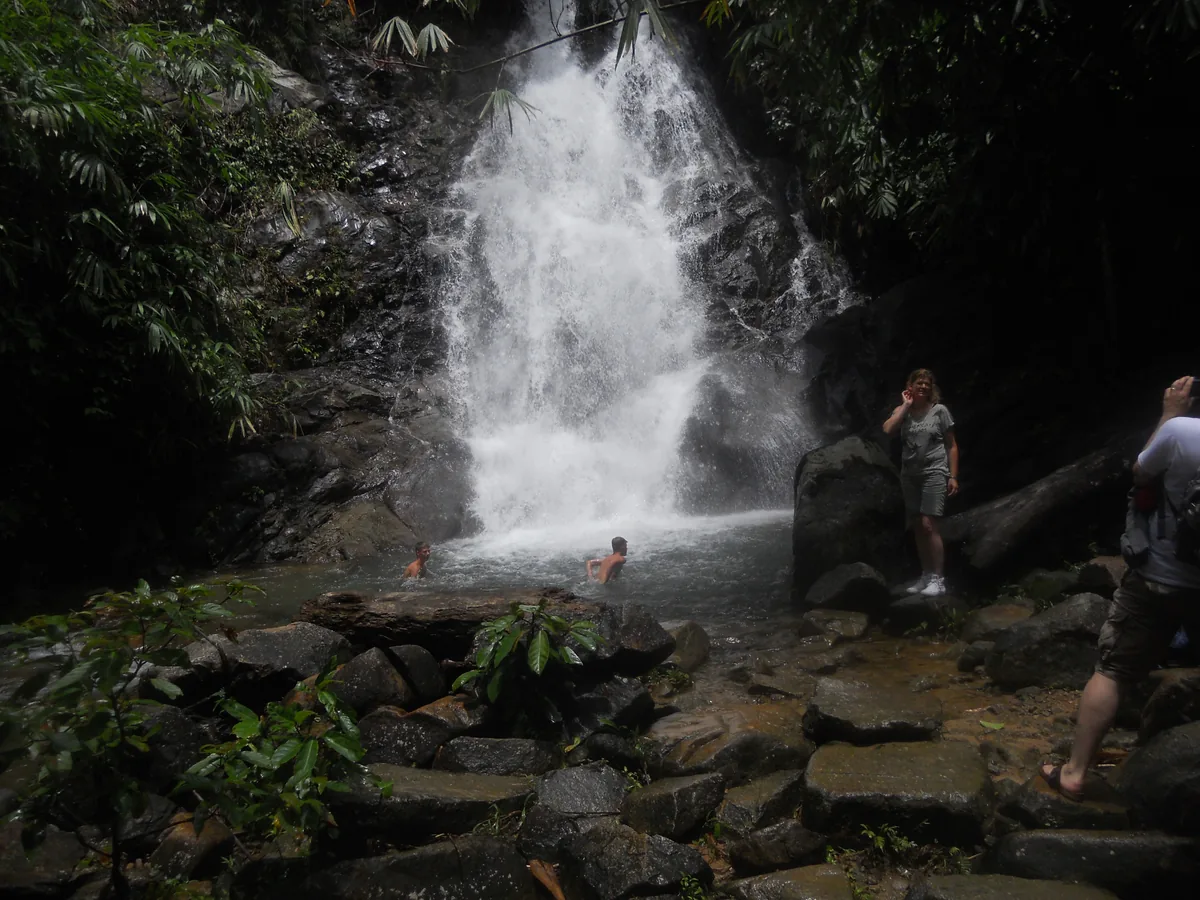 Rainbow Waterfall with visitors in the pool and on foreground rocks.