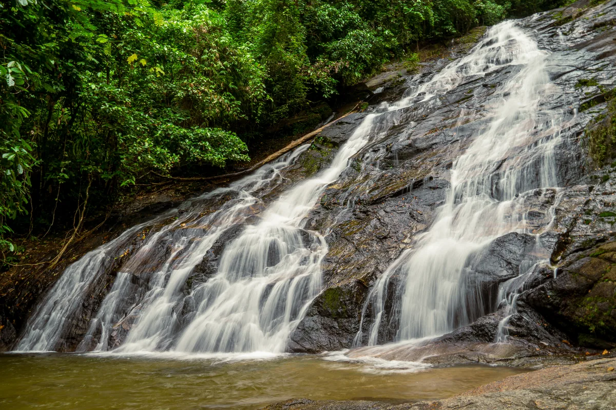 Ton Phrai Waterfall flowing across a wide rock face surrounded by rainforest