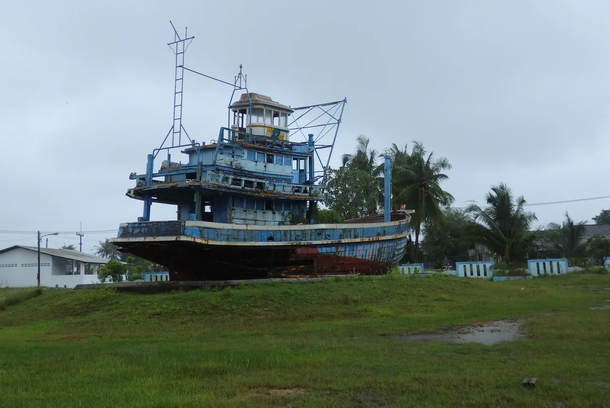 Preserved blue fishing boat displayed outdoors at Ban Nam Khem
