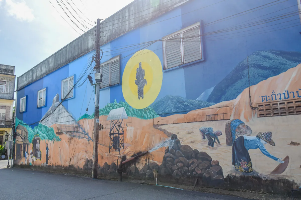 Painted street mural showing people at work on a blue wall in Takua Pa Old Town